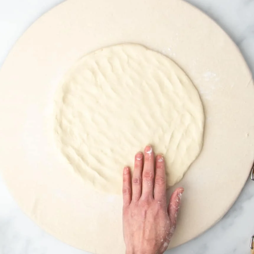 same dough with hand pressing into a thinner, larger round