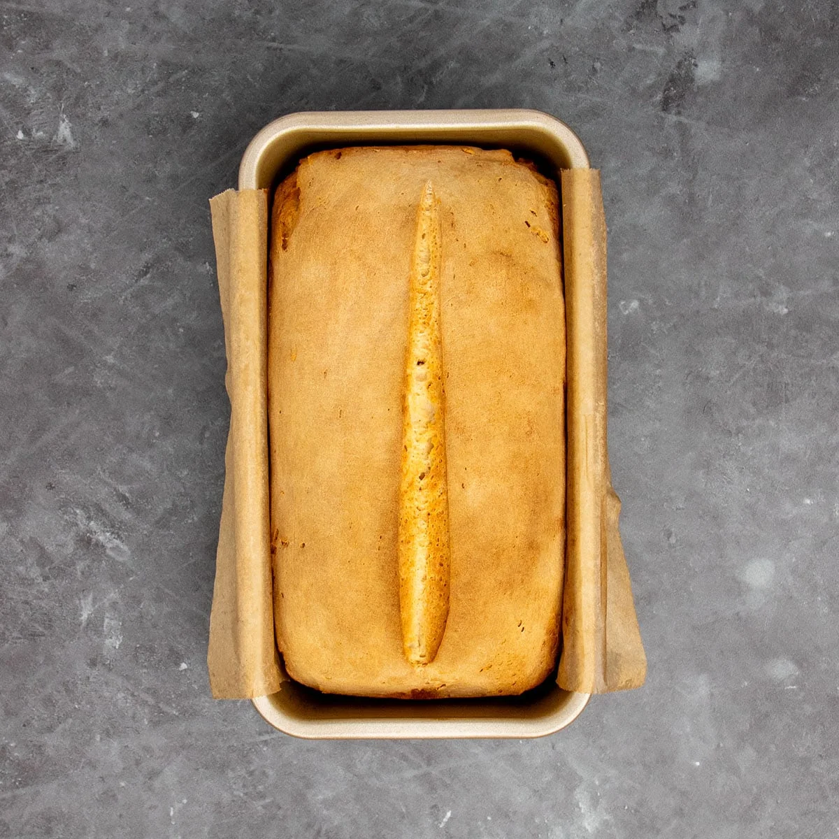 Same loaf pan with sourdough bread baked into golden brown loaf.