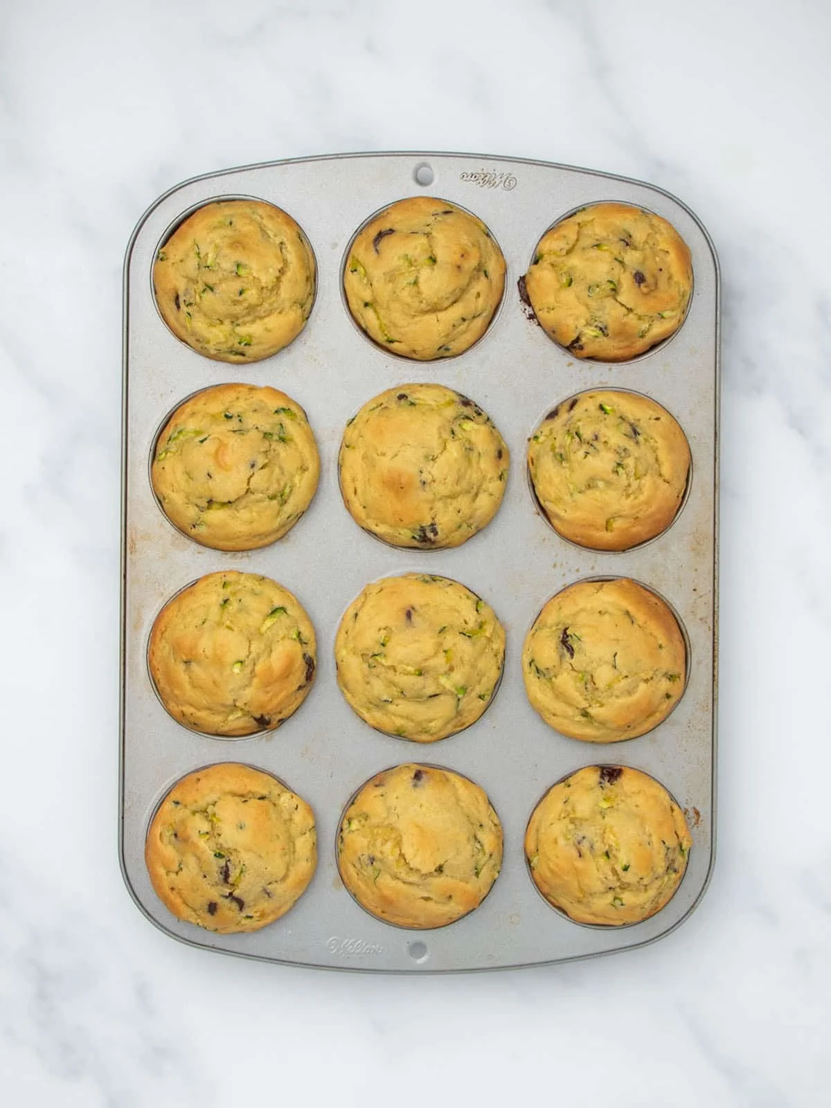 Same metal muffin tin with 12 light brown baked muffins.