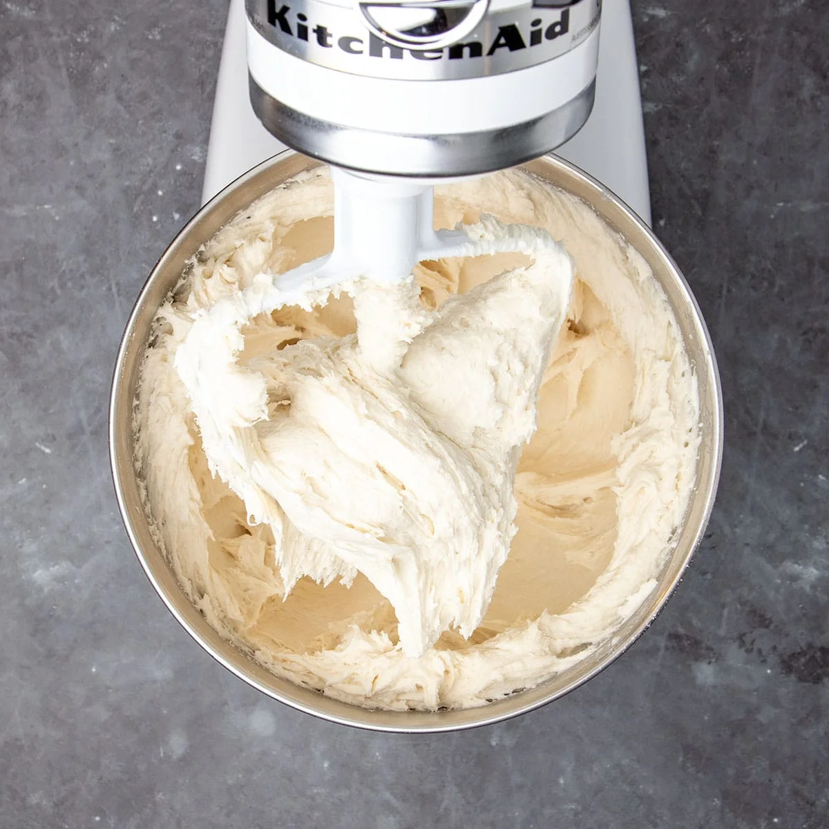 Same mixer bowl in mixer with mixer head tilted up to reveal paddle attachment with whipped-looking raw soft bread dough in bowl and on paddle.