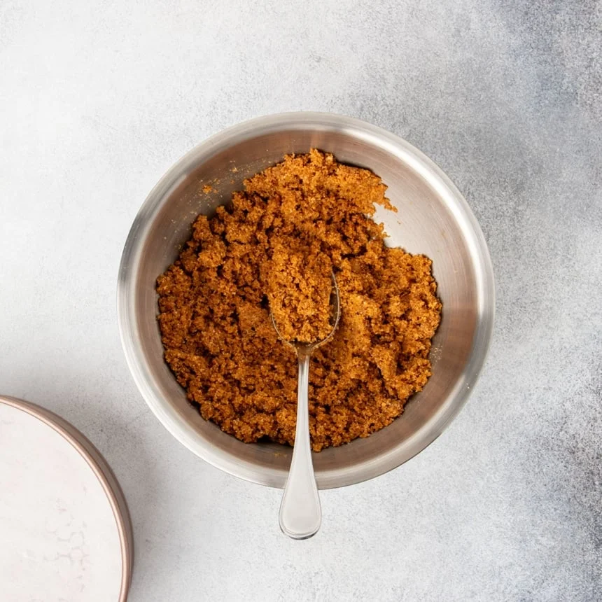Same mixing bowl with everything mixed together with a large metal spoon into dark brown wet clumps.