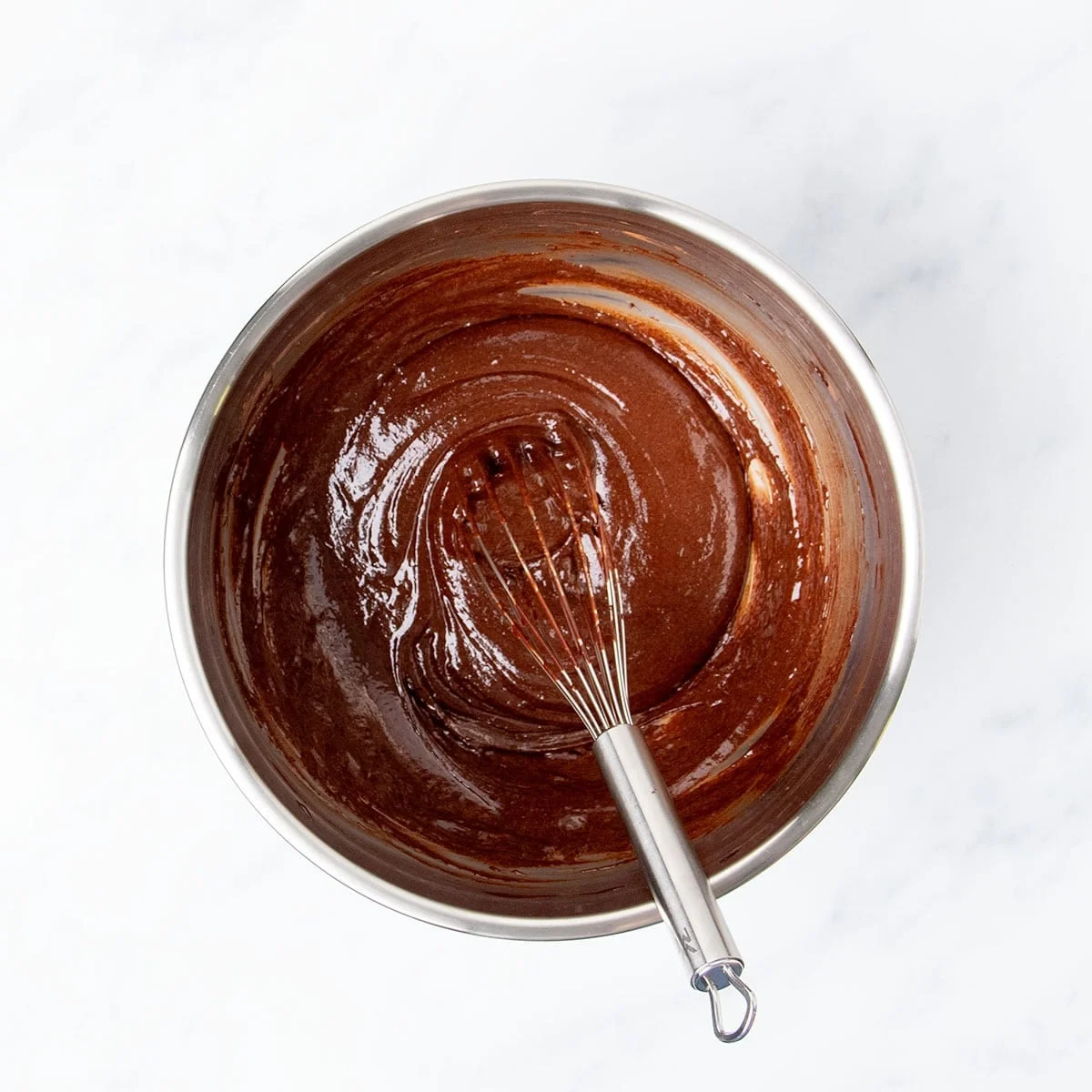 Same mixing bowl with whisked brown chocolate ingredients with wire whisk.