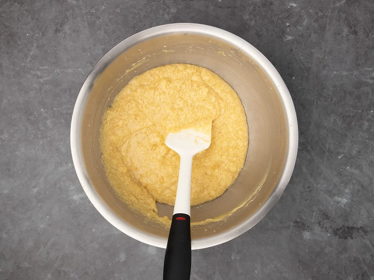 same mixture now darker yellow after mashed bananas were added, with a white spatula with a black handle