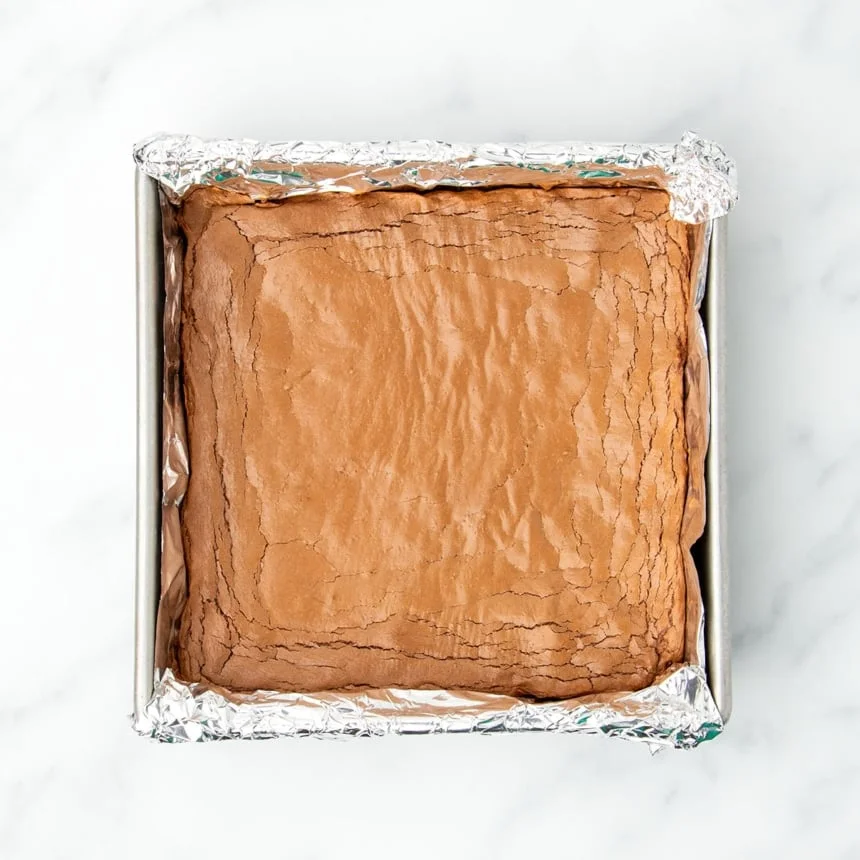 same pan with baked uncut light brown brownies with fissures demonstrating thin crinkled top
