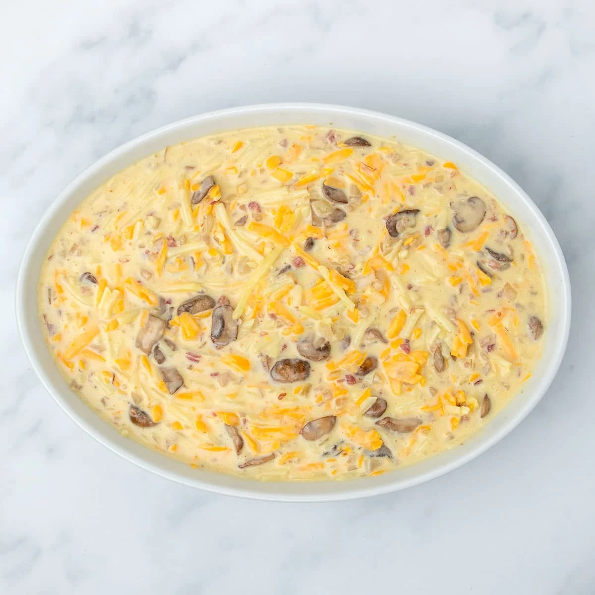 same raw breakfast casserole yellow liquid mixture with brown, yellow and pink pieces now in white oval casserole dish