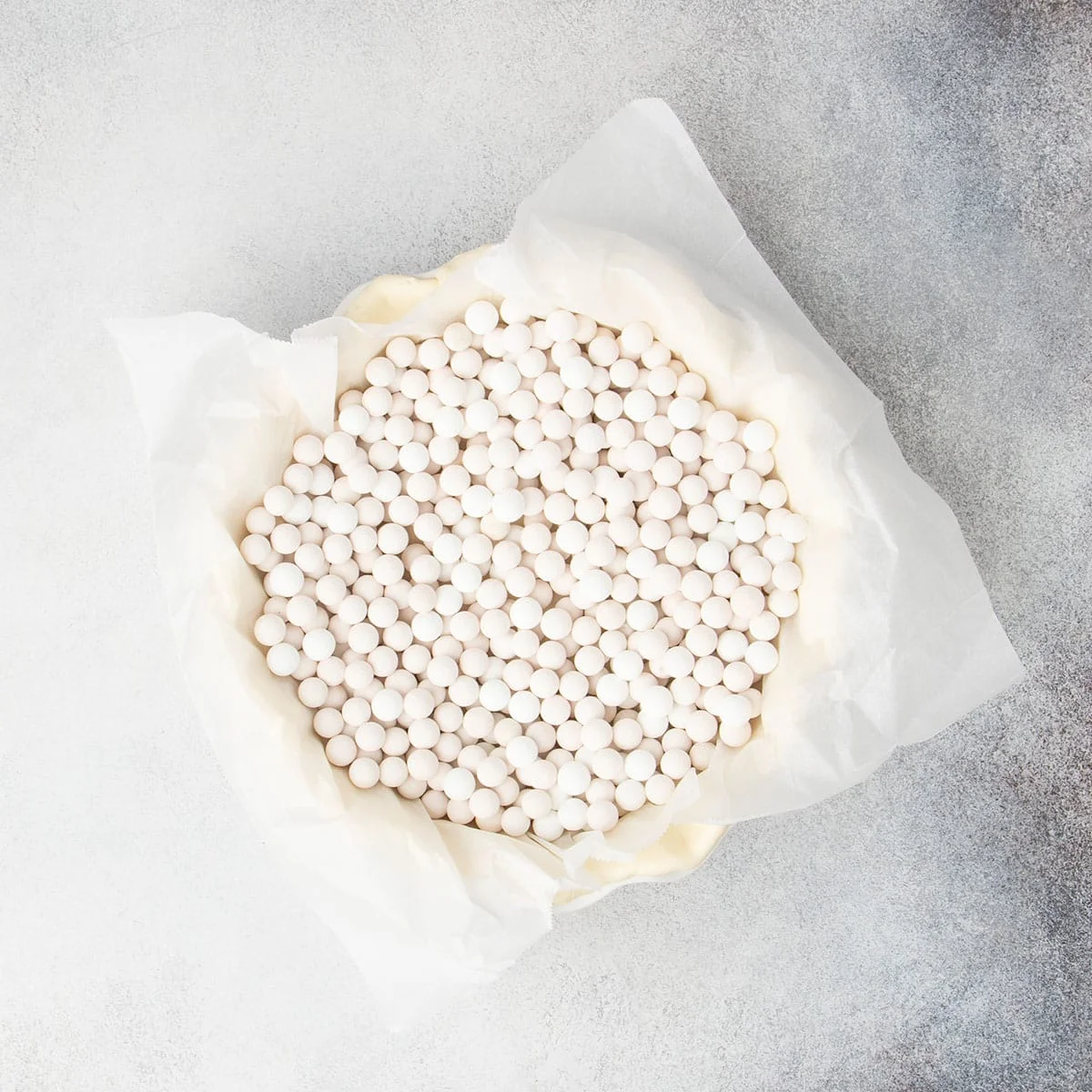 Same raw pie crust lined with white paper, which is topped with white round pie weights.