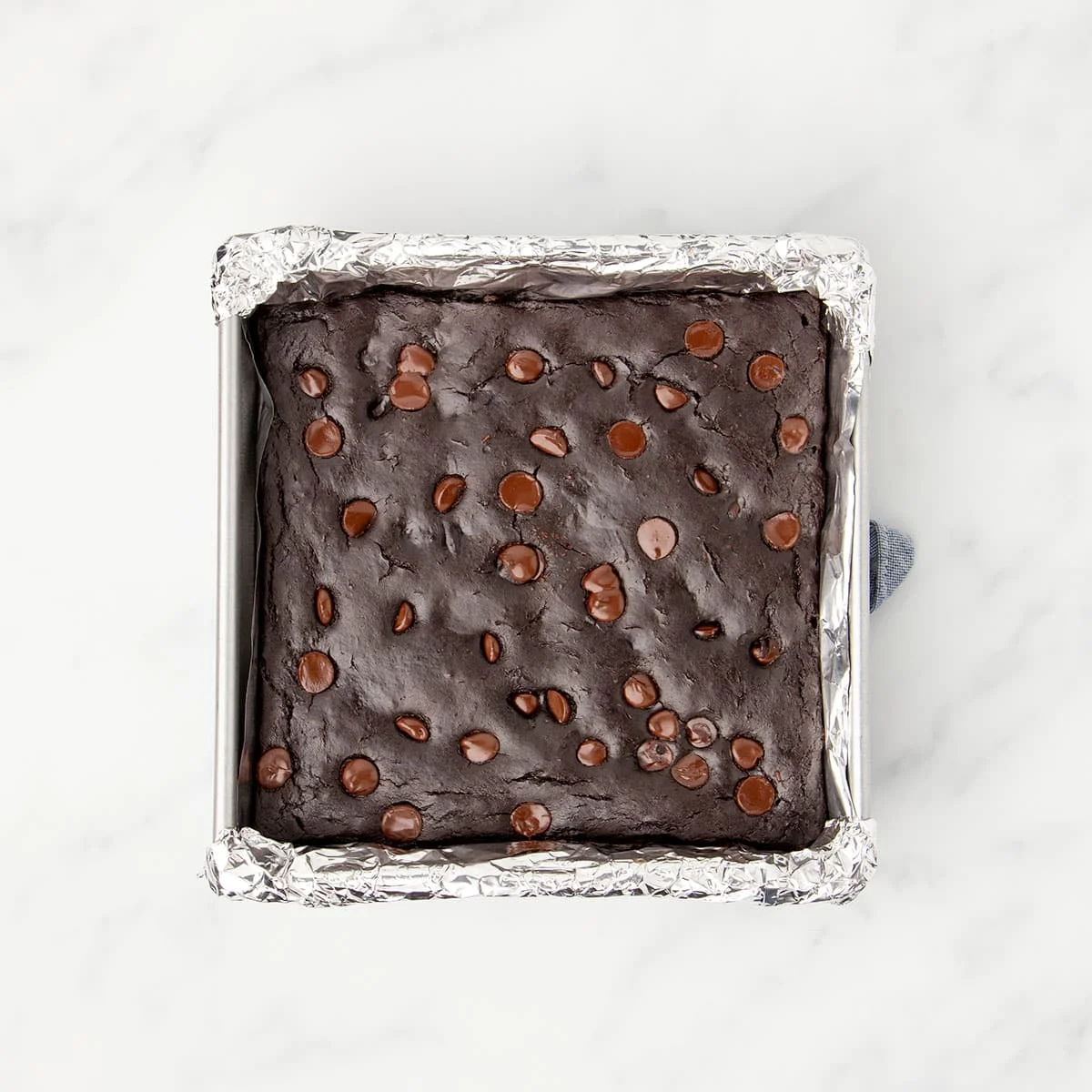 Same square baking pan with baked dark brownies with lighter brown melted chips on top.