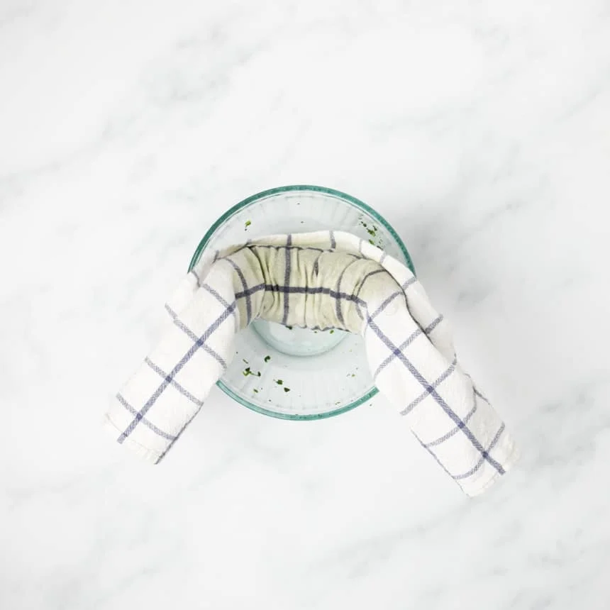 same white and blue stripe towel wrapped in cylinder around spinach and resting in small glass bowl