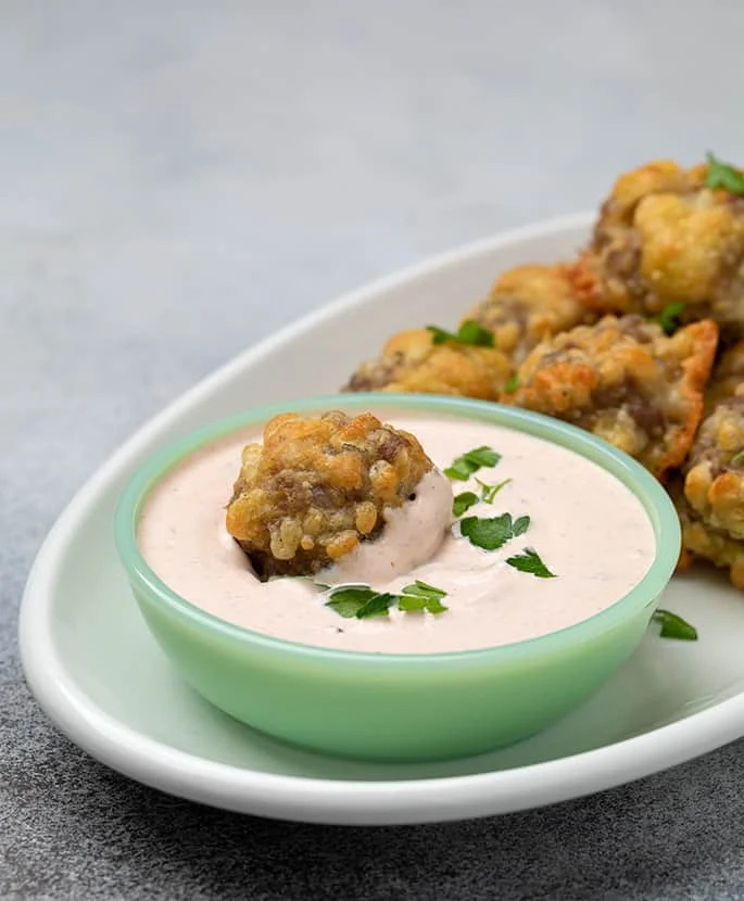 Sausage ball in light orange dipping sauce in small green bowl