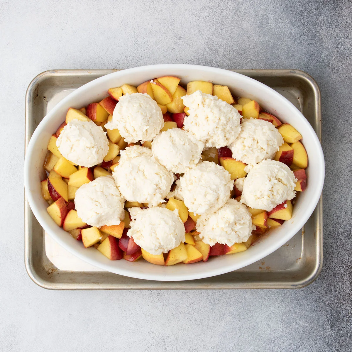 Scoops of raw topping arranged over warm peaches in the baking dish.