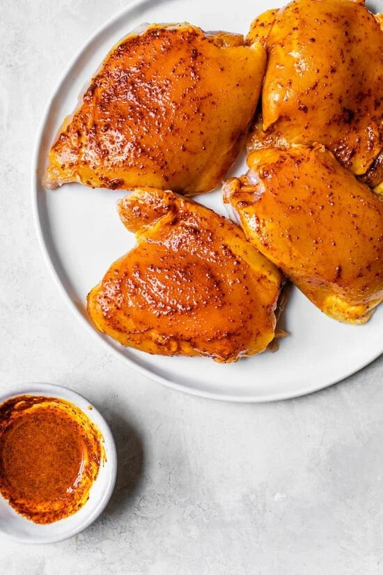 Seasoned chicken thighs marinating on a plate.