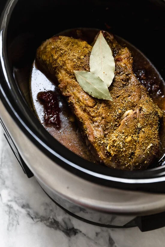 Seasoned pork shoulder in crockpot with bay leaves.