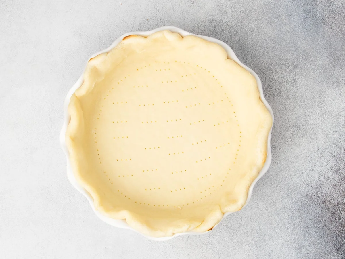 Shaped and parbaked crust in a white ceramic dish. 
