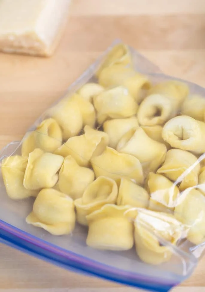 Shaped raw tortellini frozen in a zip top bag on a blond surface.