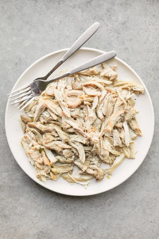 Shredded chicken next to two forks on a plate.