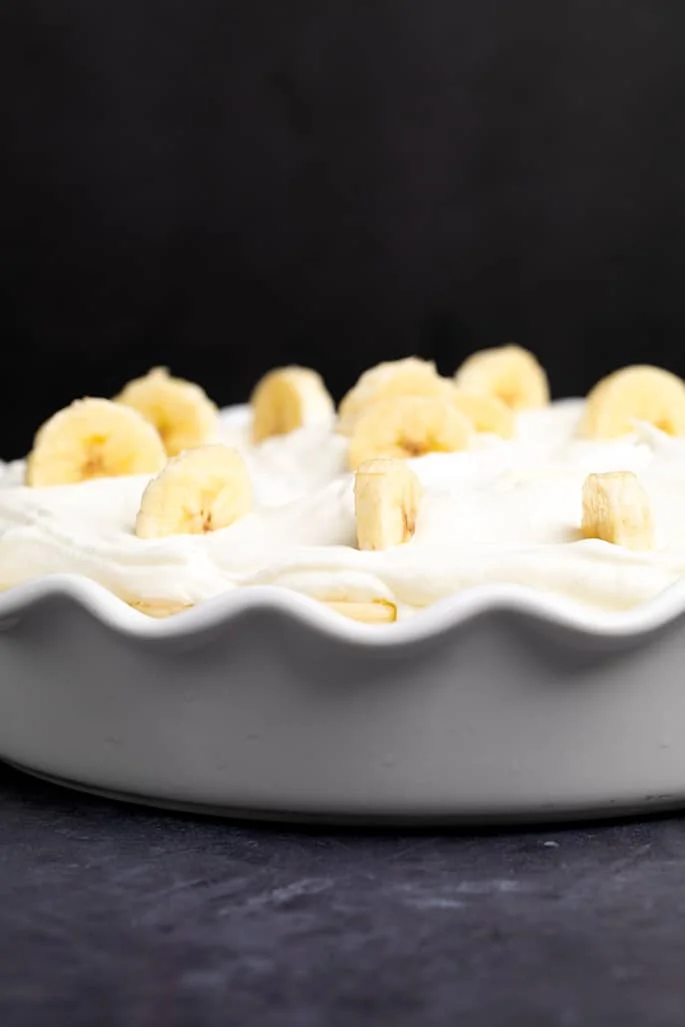 Side image of white fluted pie plate with whipped cream layer and bananas on top