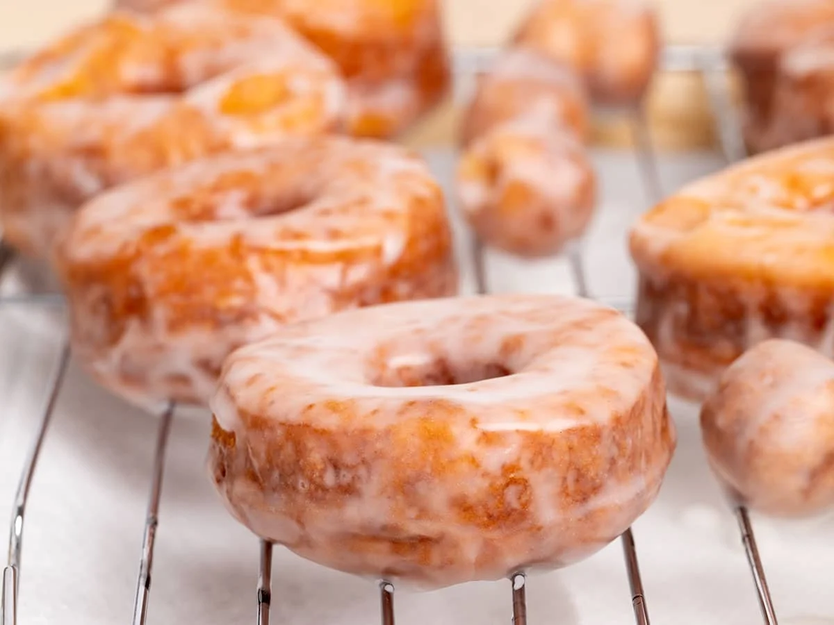 side view of brown donuts with white glaze drying on wire rack