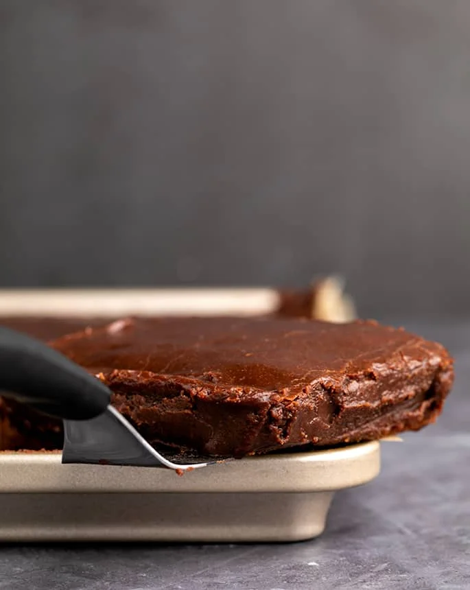 Side view of chocolate sheet cake on metal spatula in sheet pan.