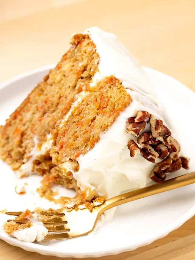 side view of slice of light brown layer cake with orange flecks and white frosting with gold form on white plate