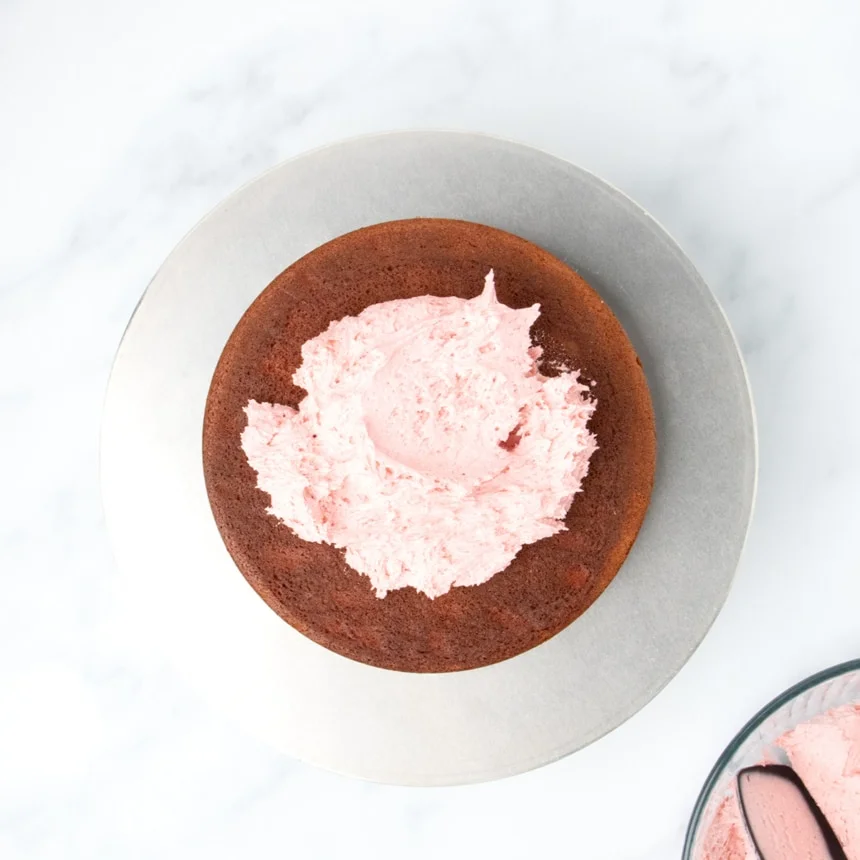 Single cake layer topped with a mound of pink frosting on a round metal turntable
