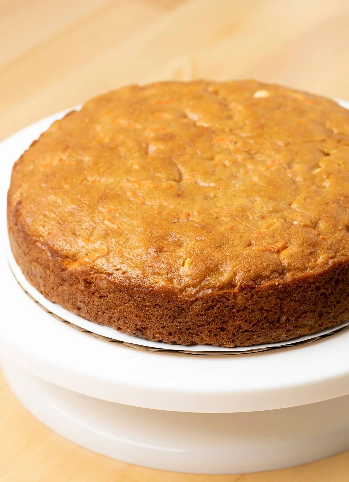 Single layer baked carrot cake on white cake turner.