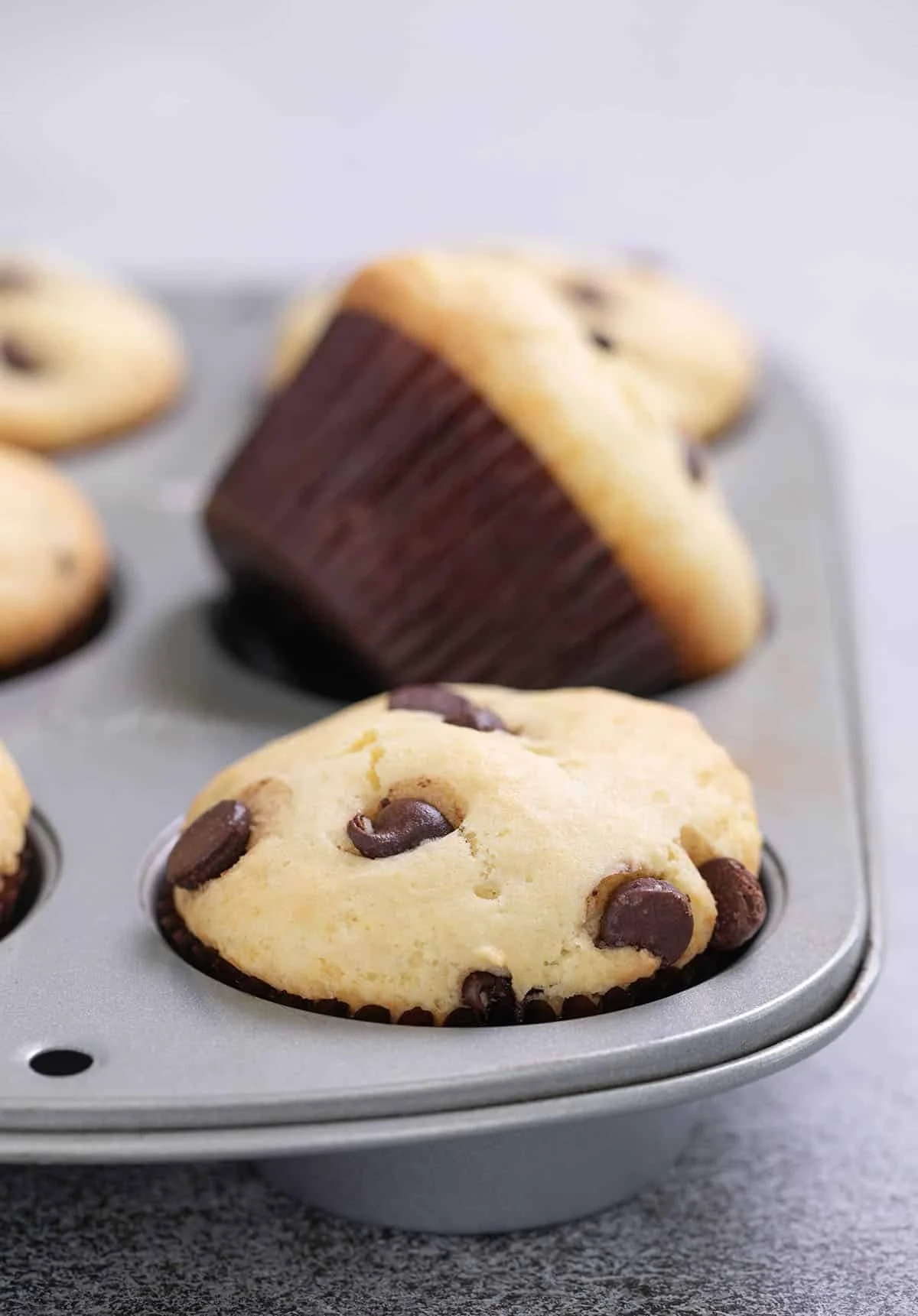 Six chocolate chip muffins in a muffin tin with one on its side