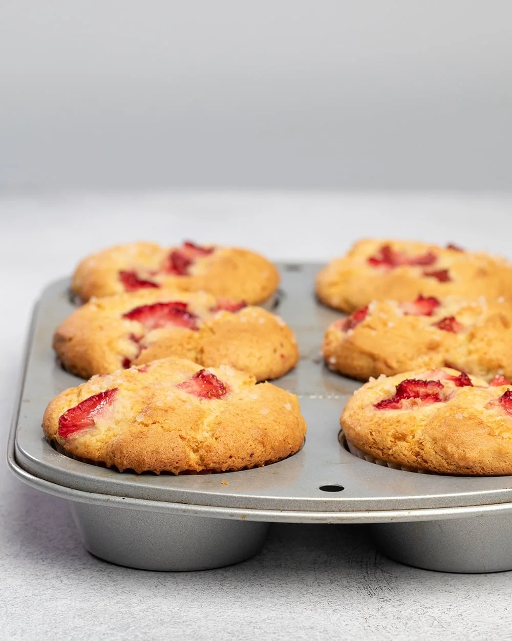 Six strawberry muffins baked in metal muffin tin.