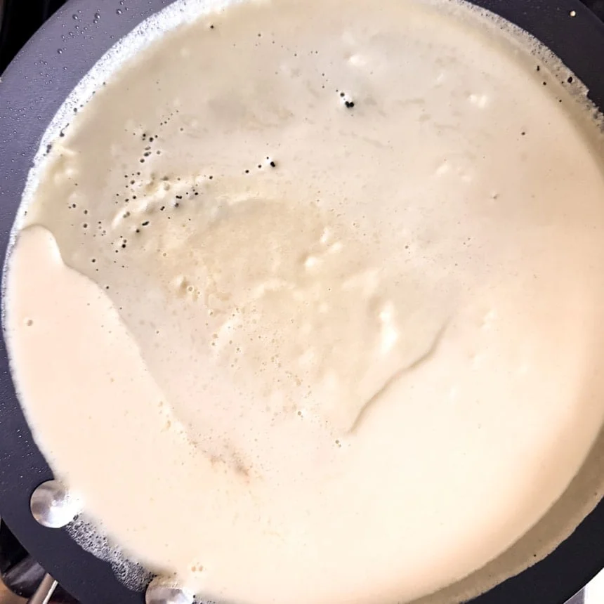 Skillet being tilted to distribute crepe batter evenly, with bubbles forming across the surface.