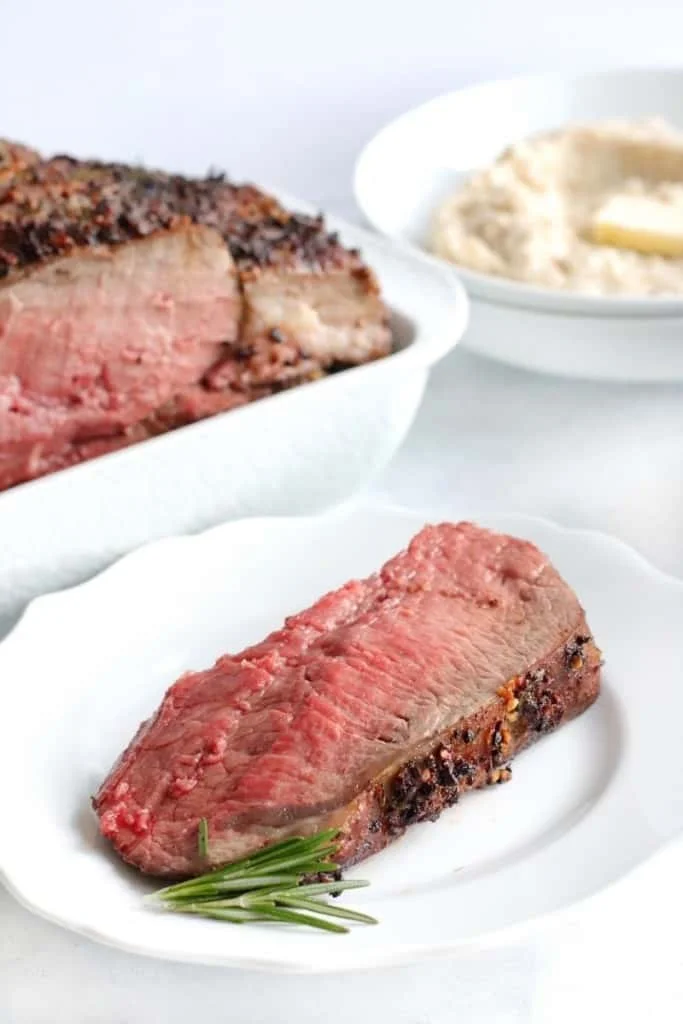 Slice of air fryer prime rib on a white plate with a side of rosemary plated with it