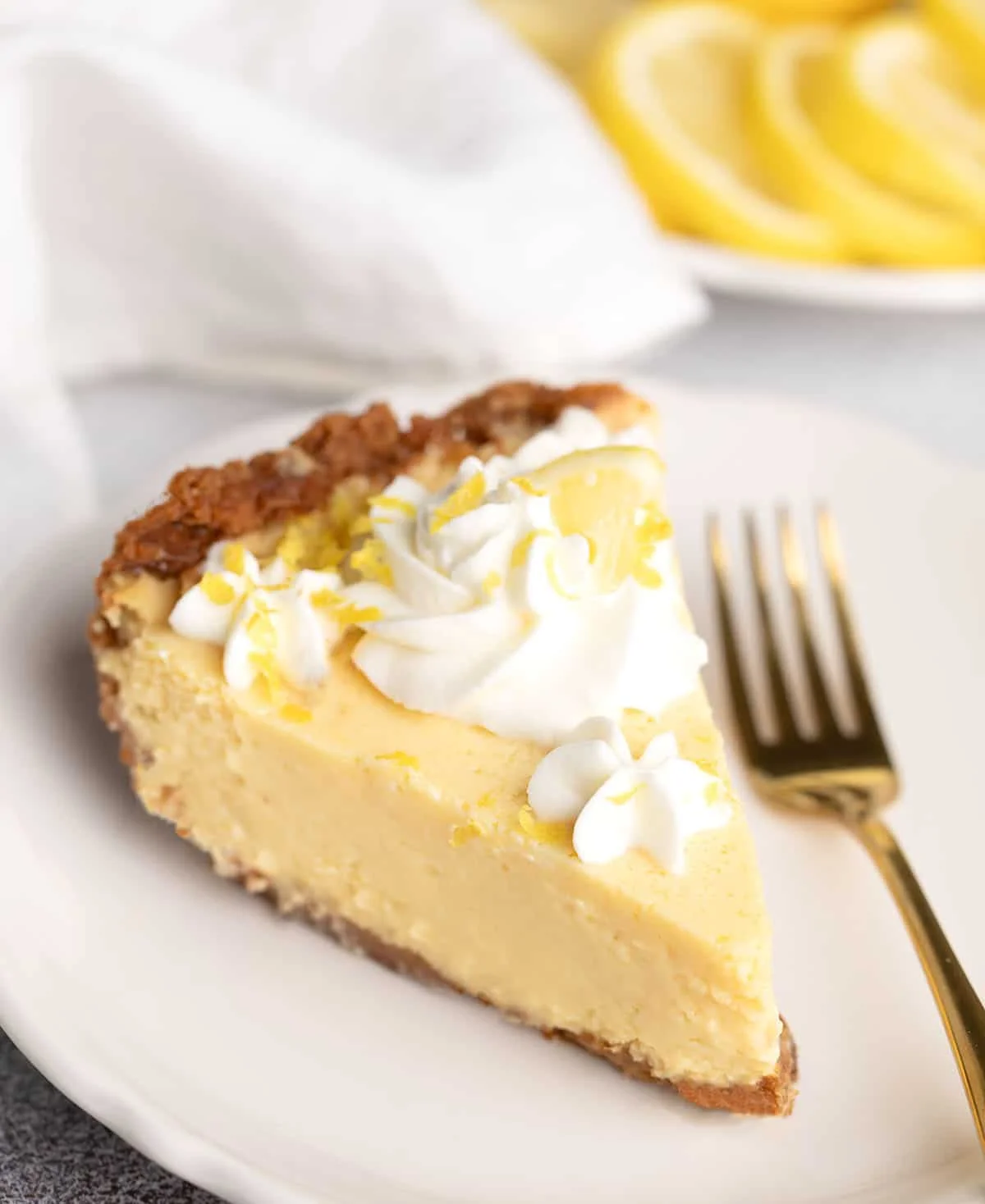 Slice of chilled lemon pie topped with whipped cream and lemon zest, served with a gold fork