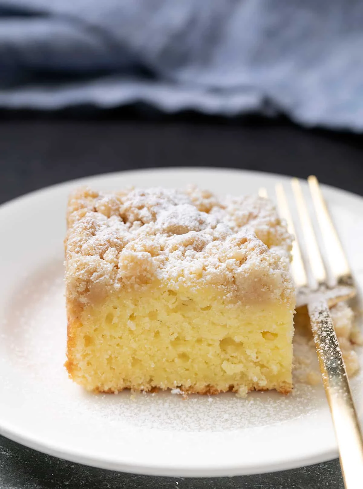 slice of gluten free coffee cake with powdered sugar on white plate with fork