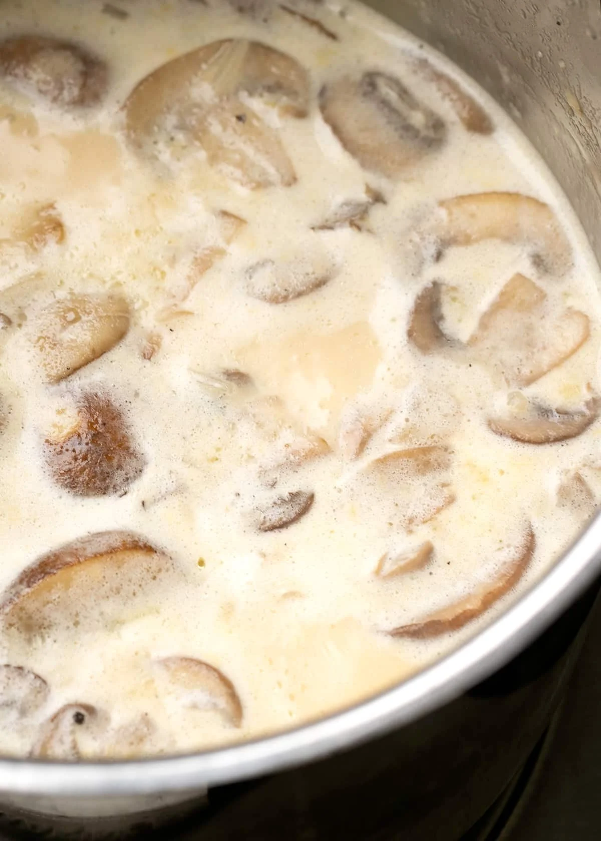 sliced cooked mushrooms in creamy soup in metal saucier pan