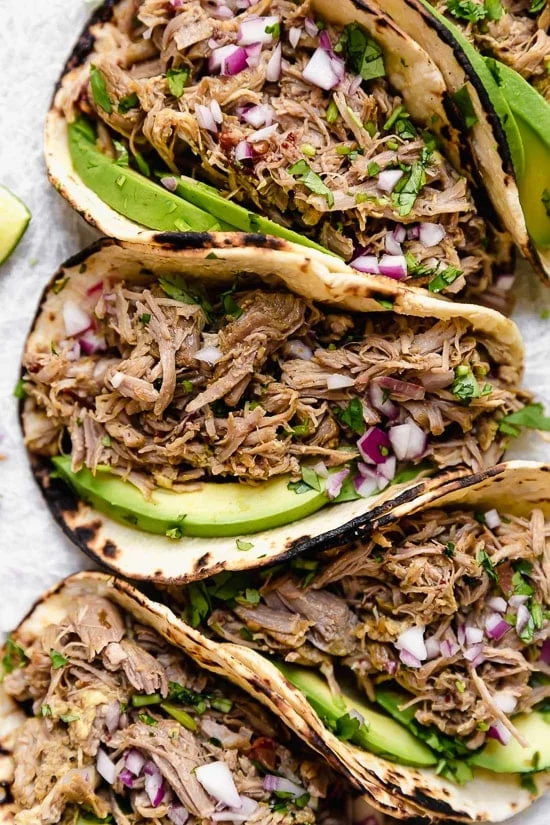 Slow cooker carnitas tacos with avocado slices.