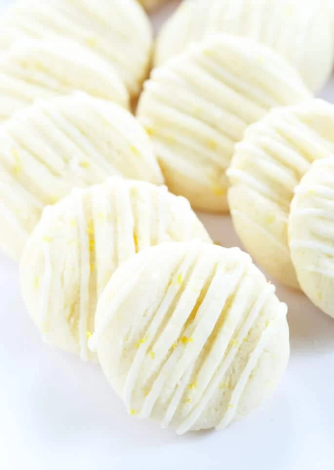 Small light white cookies with flecks of bright yellow with stripes of white icing, leaning against each other on a white surface 
