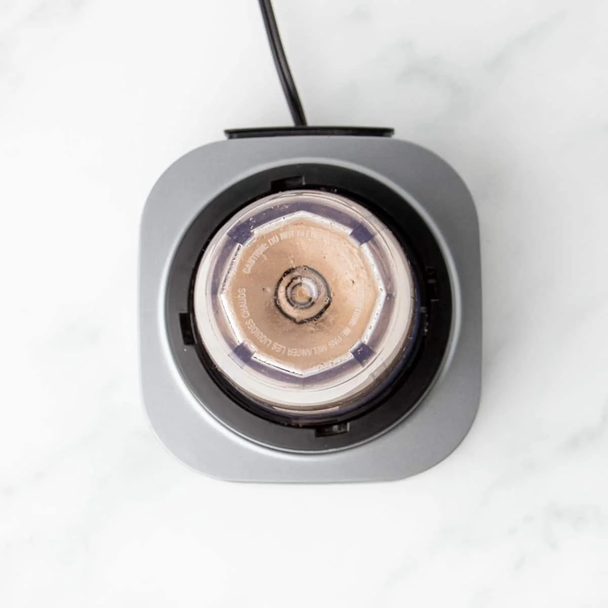Small magic bullet blender canister on silver base with light brown mixture being blended inside canister.