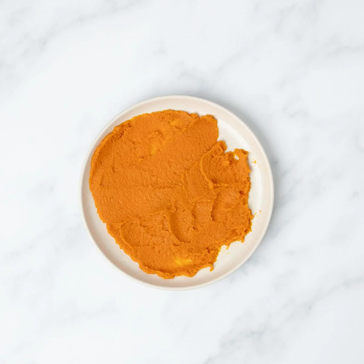 small round dessert plate with orange pumpkin puree spread into even layer