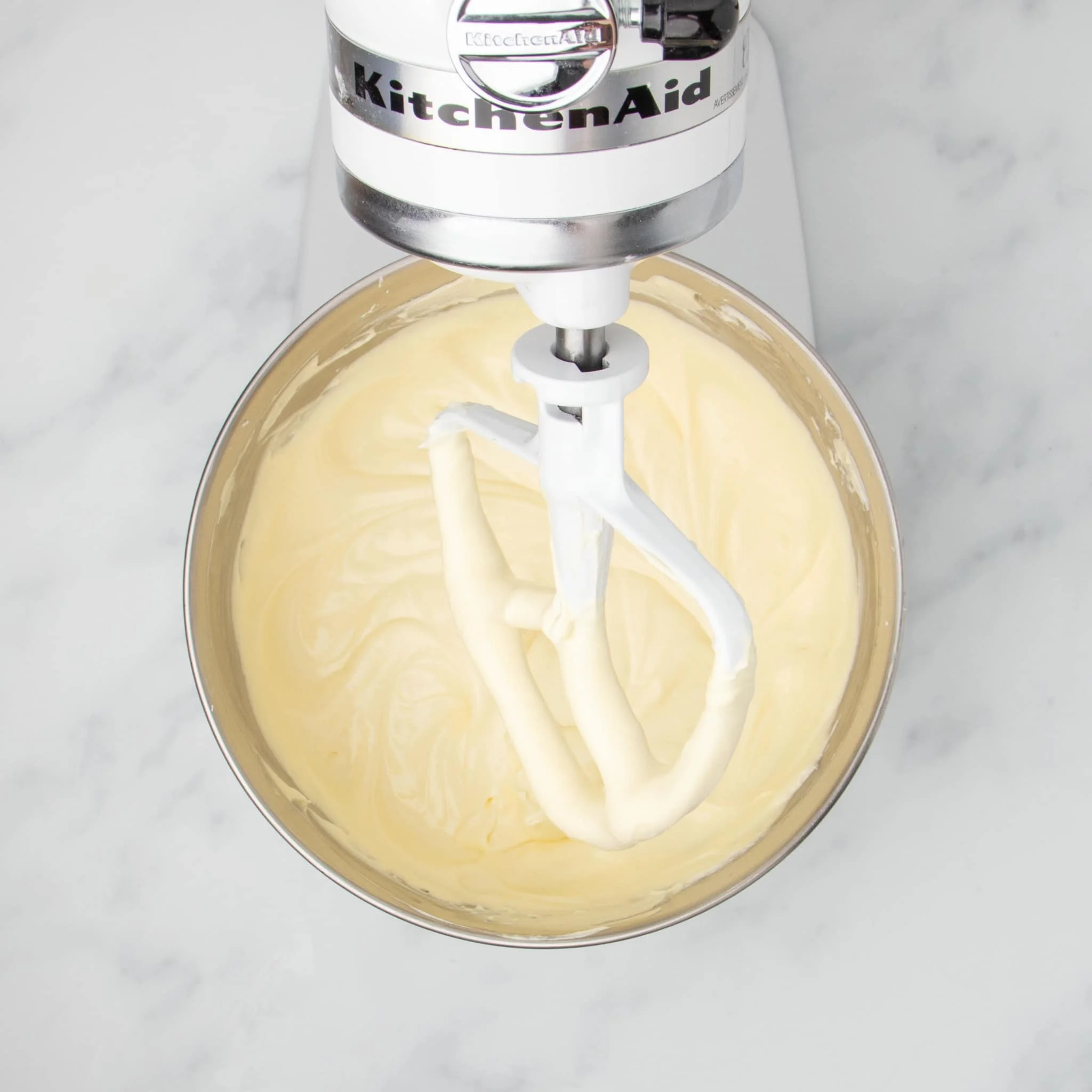 smooth light yellow raw cheesecake mixture in mixing bowl with white paddle