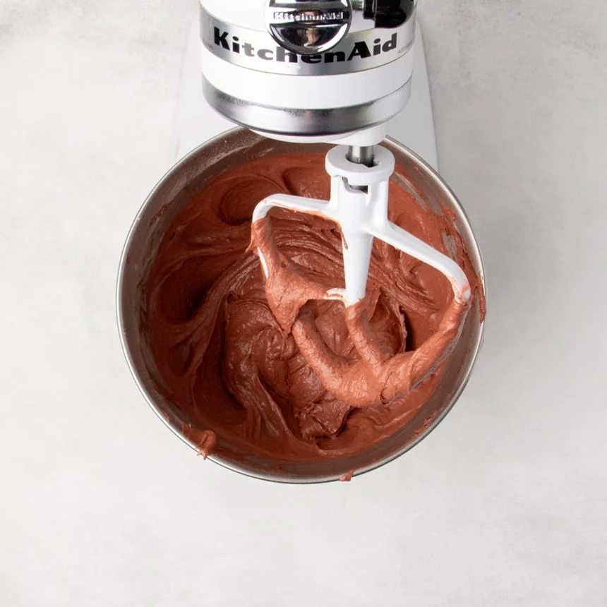Smooth reddish chocolate-colored batter in a stand mixer bowl with a paddle attachment lifted above the batter.