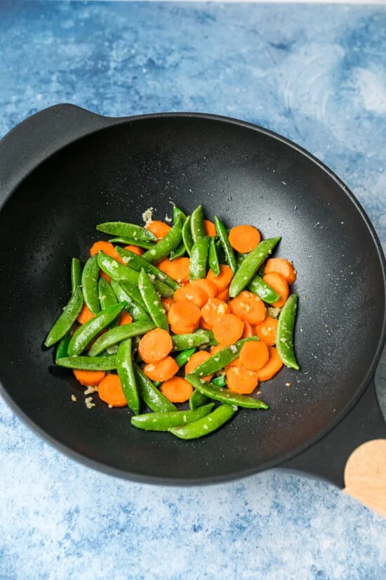 Snap peas and carrots sautéed with ginger and garlic in a wok.