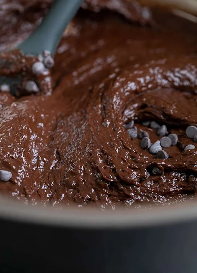 Soft brown batter with miniature chocolate chips with black mixing spoon in metal bowl