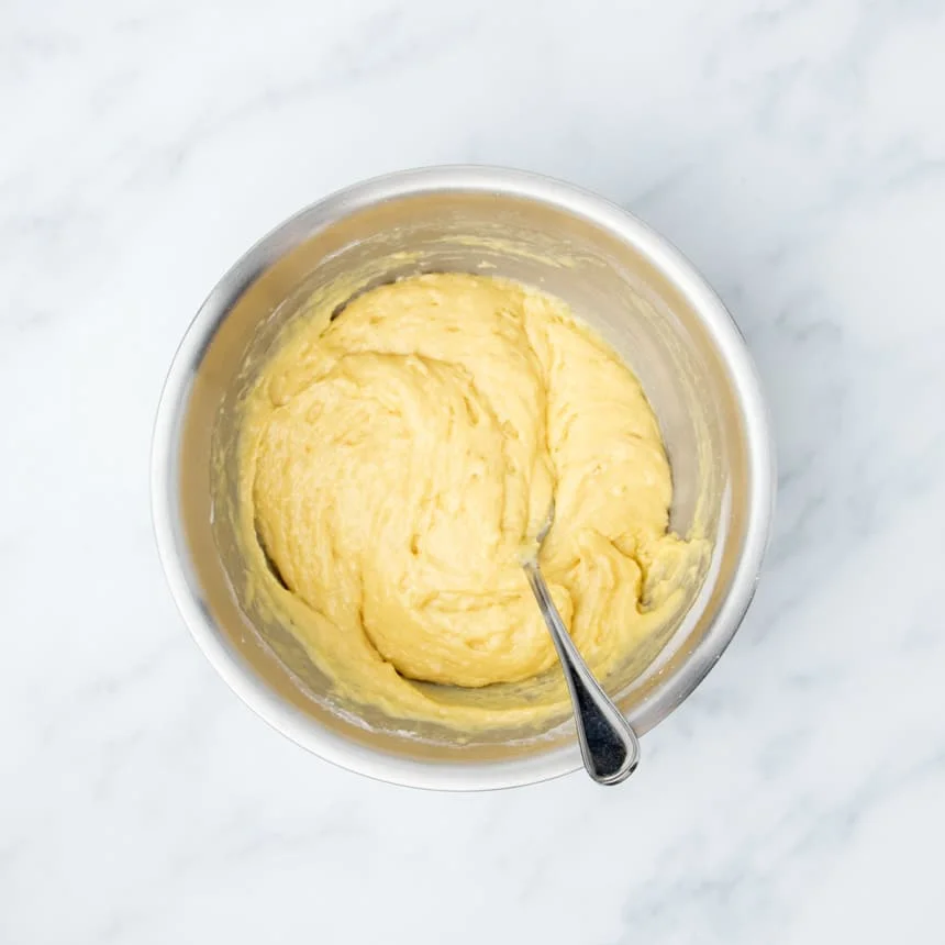 soft yellow mixture of muffin batter in same metal round mixing bowl with metal mixing spoon