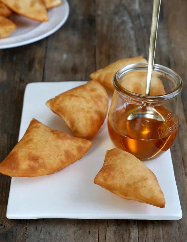 Sopapillas on white plate with jar of honey 