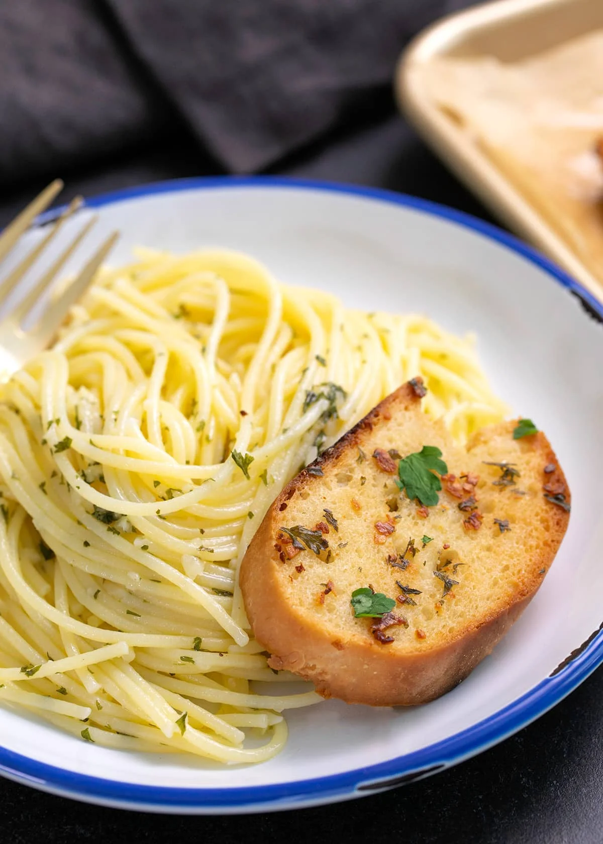 Spaghetti on a white plate with a fork and a piece of garlic bread