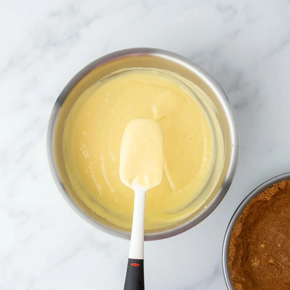 Spatula resting in a bowl of smooth lemon filling, ready to be poured into the crust.