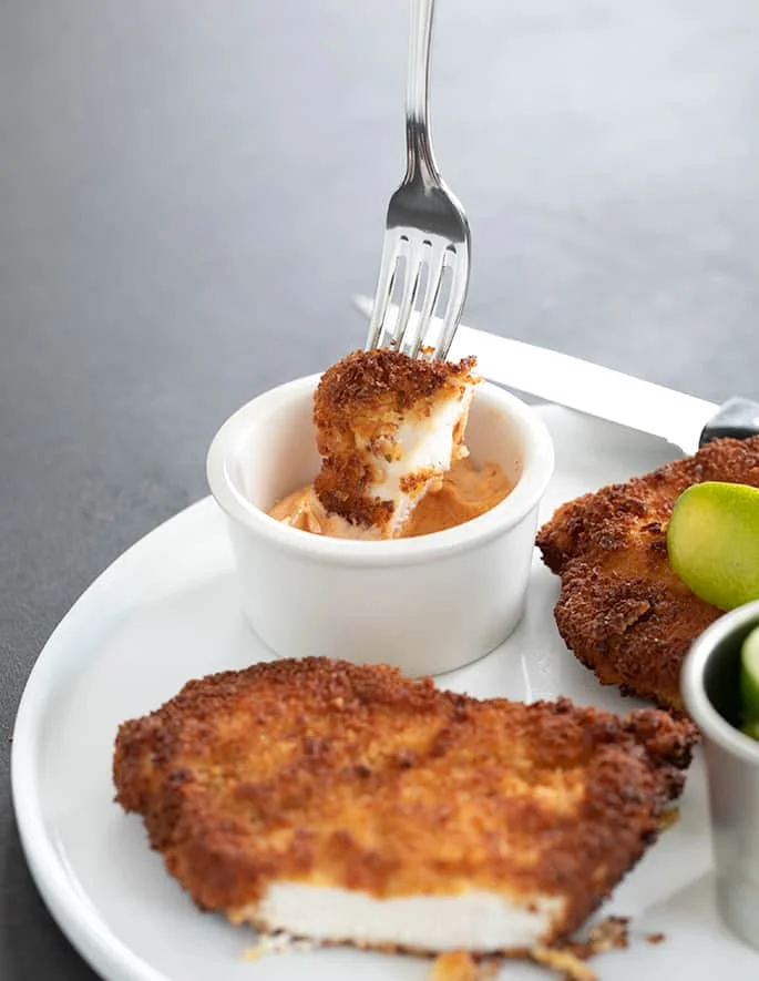 Spicy chicken cutlet piece being dipped in sauce