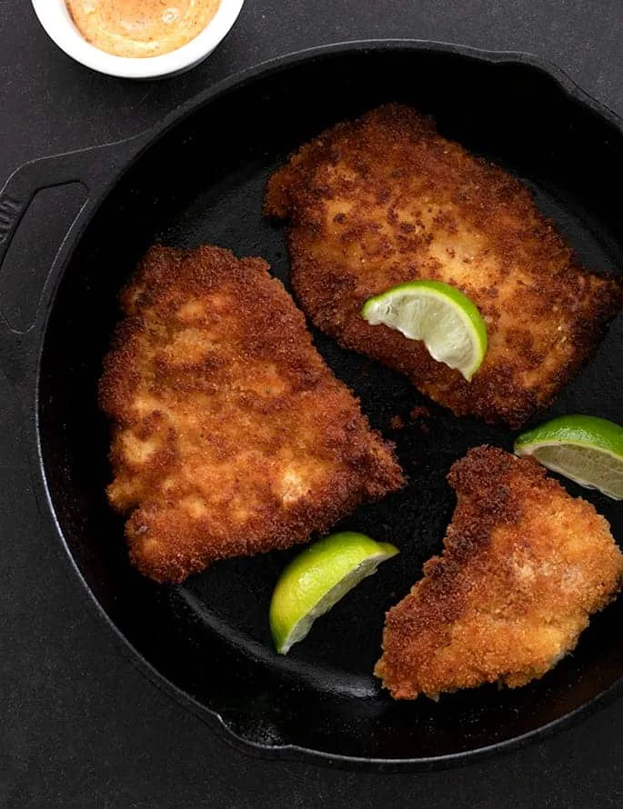 Spicy chicken cutlets in pan with limes overhead image