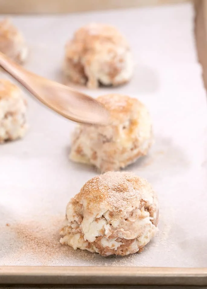 Spoon sprinkling cinnamon sugar on raw mound of cinnamon sugar biscuit
