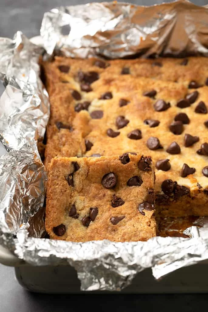 Square of pumpkin dump cake with chocolate chips leaning against rest of cake in foil lined baking pan