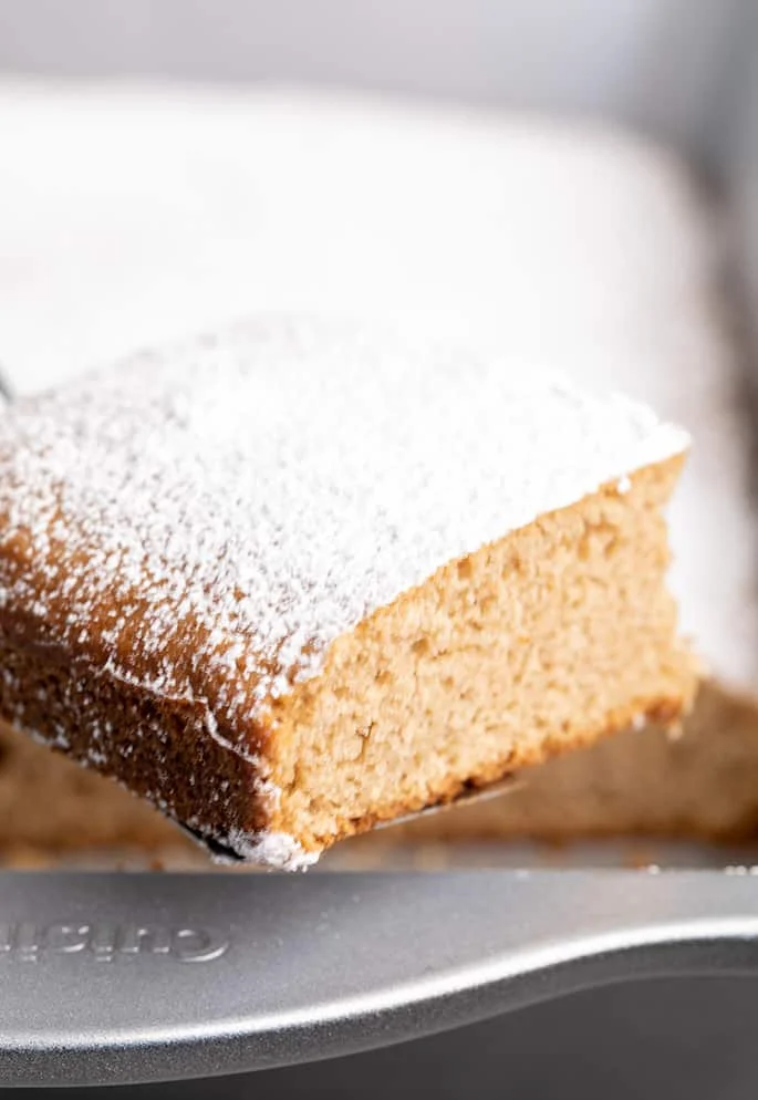 Square slice of spice cake with powdered sugar being lifted out of pan