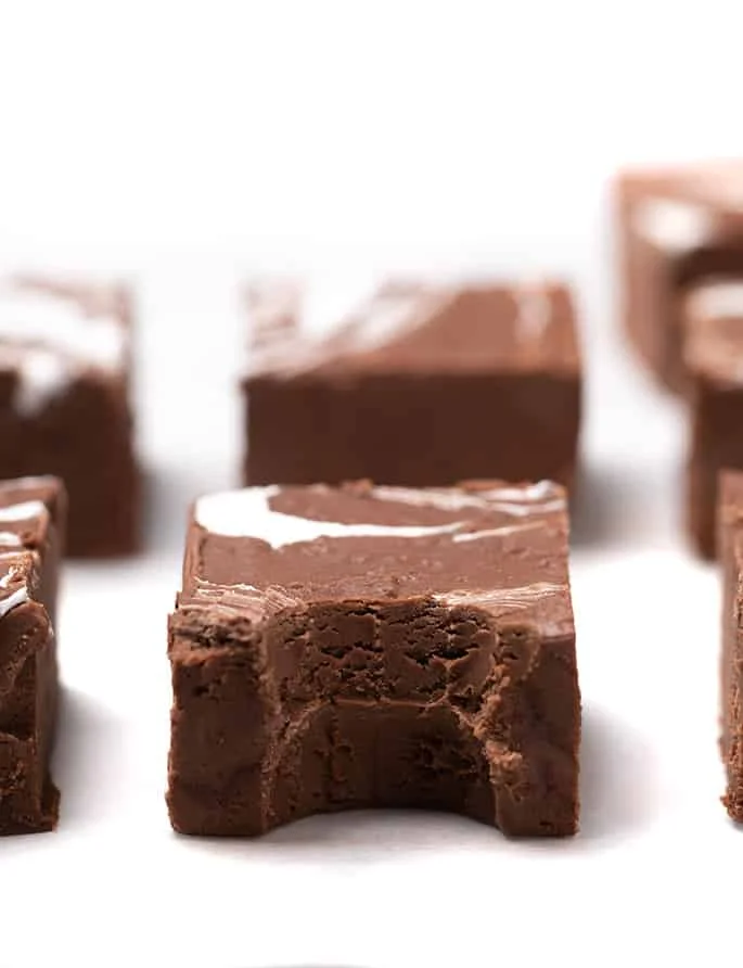 Squares of brown fudge on white paper, piece in center with bite taken